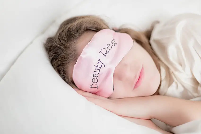 une femme dort dans un lit avec un masque de nuit rose sur les yeux